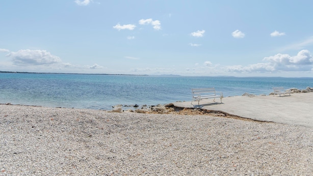 Egy kavicsos strand, egy pad és sziklás parttal.