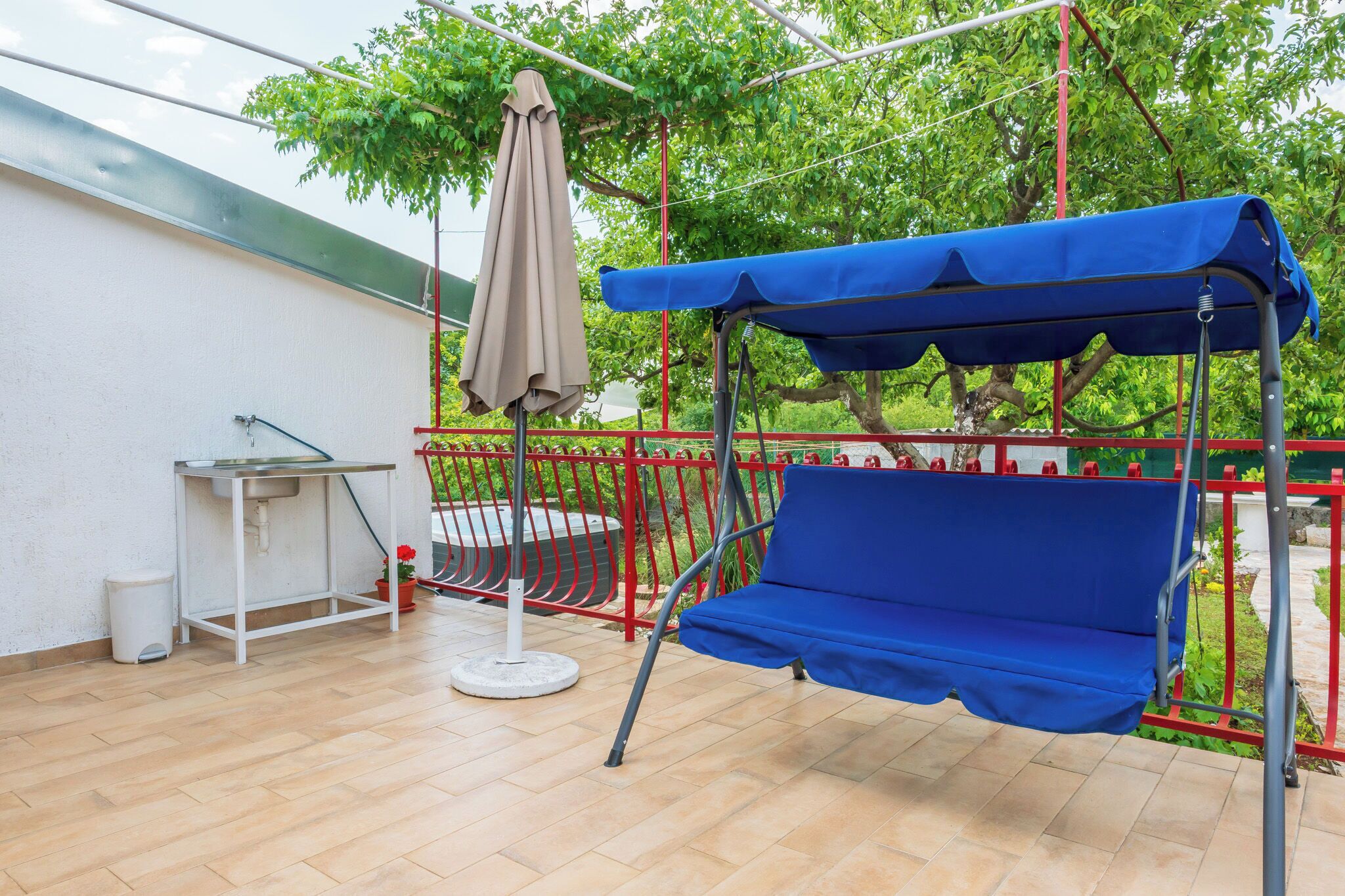 A balcony with a blue swing, a white table with a sink, and a beige umbrella.