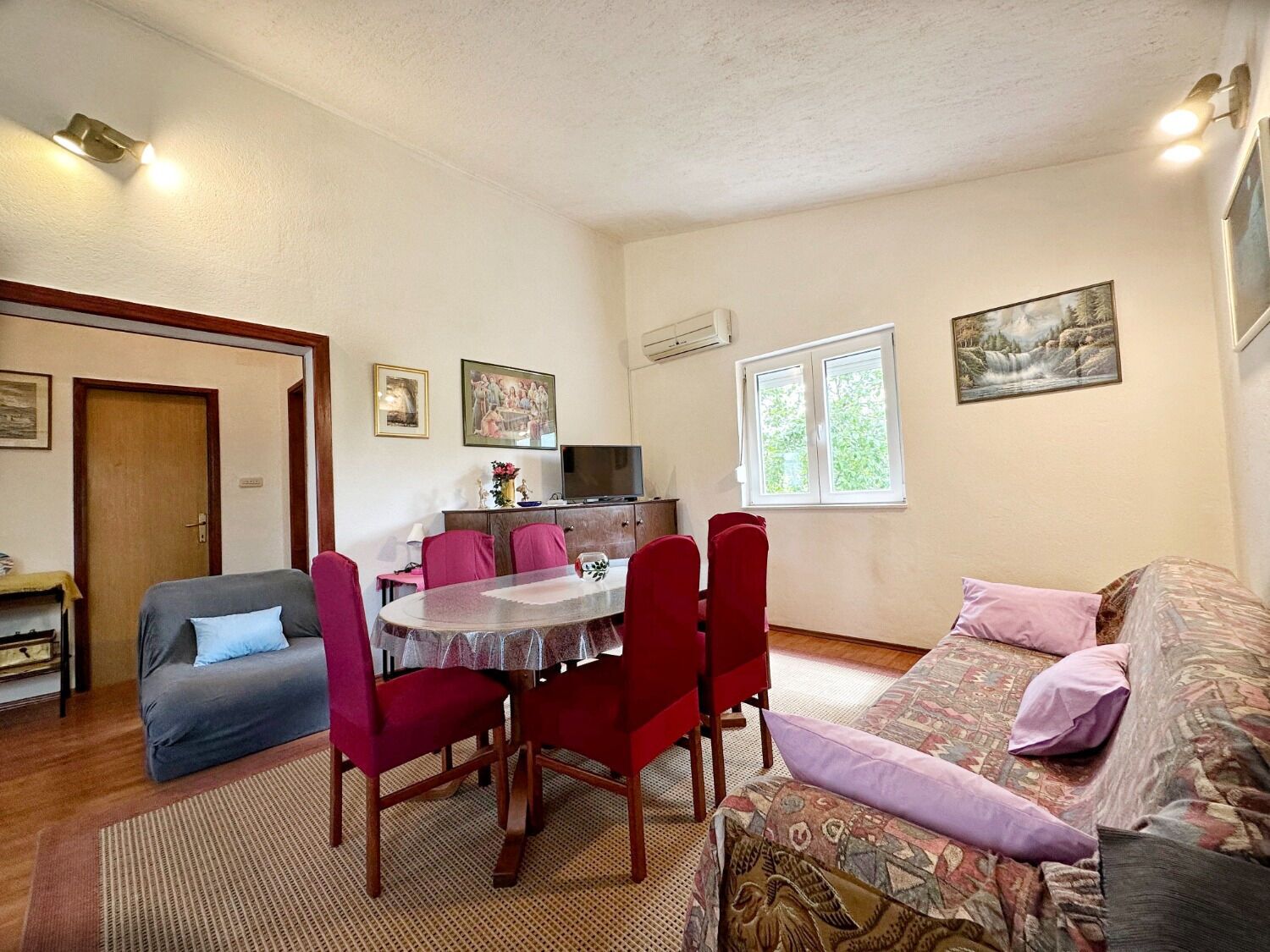 A cozy living room with a dining area, a sofa, a TV, and a window with a view.