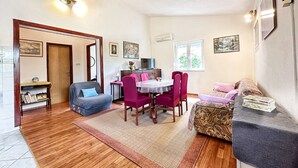 A cozy living room with a sofa, a dining table with chairs, a TV, and a bookshelf. - House Tamy - With Jacuzzi (Omis)