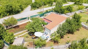 A residential building with a red-tiled roof, a fenced garden, and a visible road. - House Tamy - With Jacuzzi (Omis)