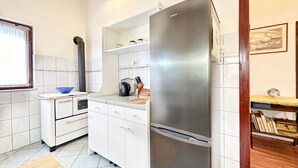 A compact kitchen with white cabinets, a stainless steel refrigerator, a small stove, and a window with curtains. - House Tamy - With Jacuzzi (Omis)