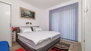 Ein Schlafzimmer mit einem Bett, einem Gemälde, einem Fenster mit Jalousien und einem roten Teppich.