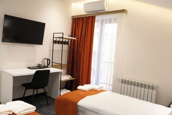 Ein Hotelzimmer mit Bett, Schreibtisch mit Stuhl, Fernseher, Klimaanlage, Heizkörper und Vorhängen.