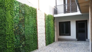 A courtyard with a tiled floor, a green hedge, and a building with a balcony. - New Casa  (Yerevan)