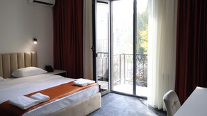 A hotel room with a bed, a desk, a chair, a balcony with a view, and an air conditioning unit. - New Casa  (Yerevan)