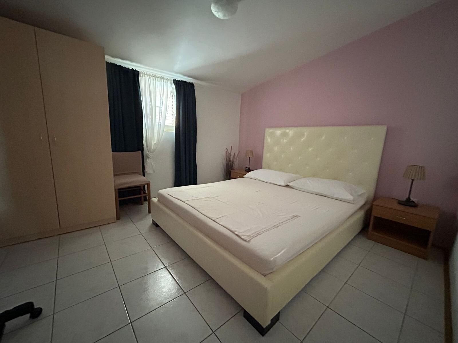 A bedroom with a large bed, a wardrobe, a chair, and a nightstand with a lamp.