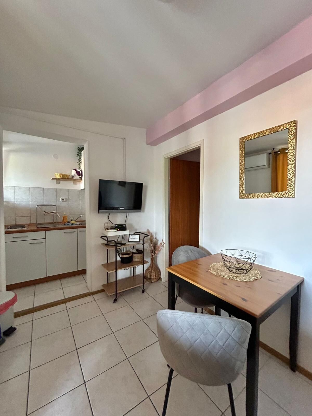 Een compacte keuken met witte kasten, een televisie en een eethoek met een tafel en stoelen.