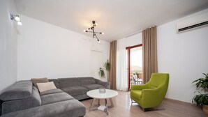 A modern living room with a grey sectional sofa, a white coffee table, a green armchair, and a potted plant. - Apartment Val (Okrug)