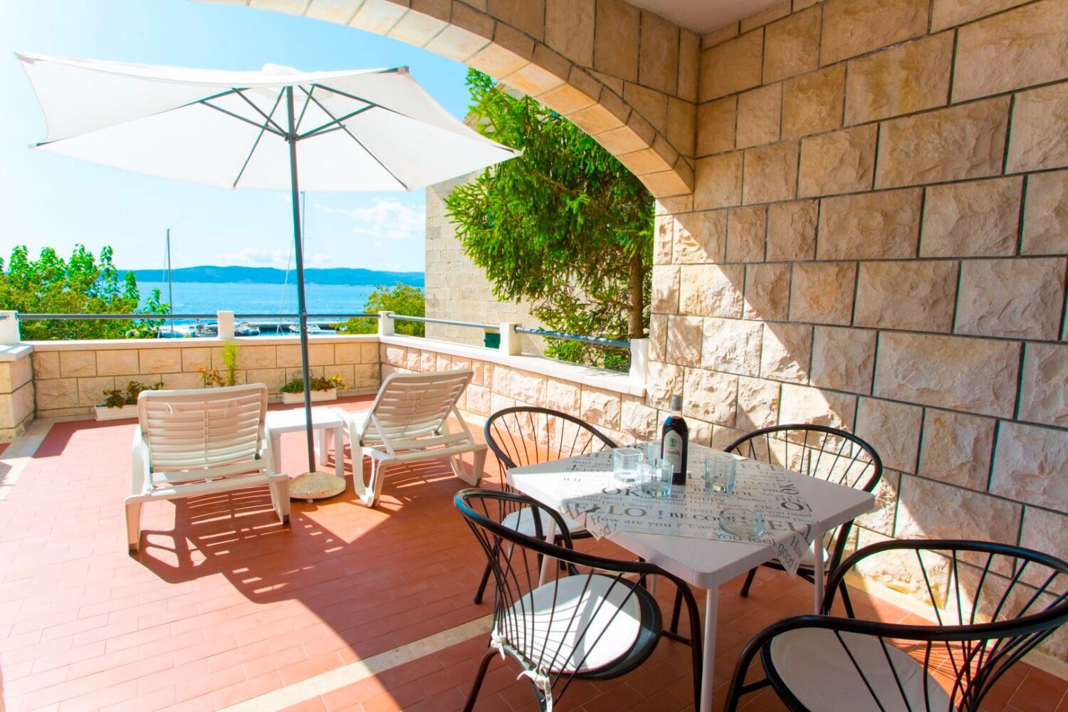 Una terraza con mesa y sillas, un paraguas blanco y vista al mar.