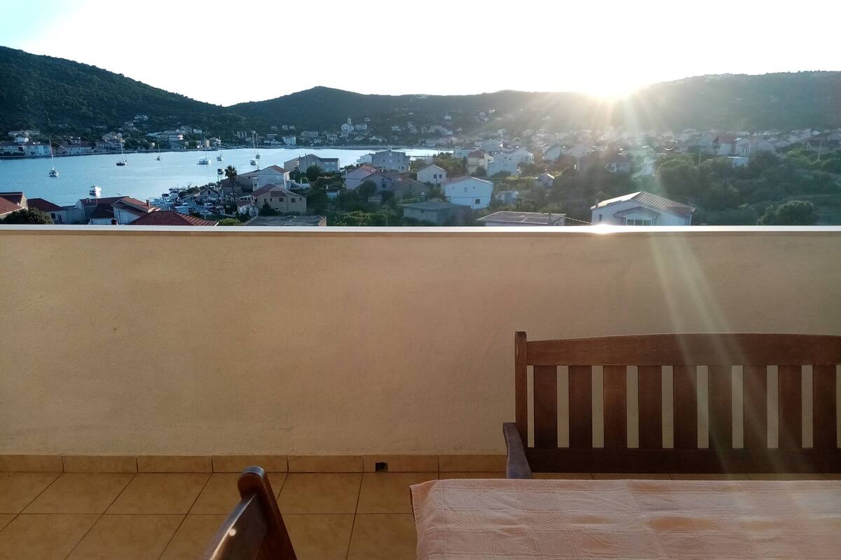 A balcony with a view of a coastal town, a table, and two chairs.