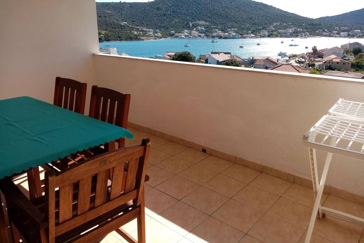 A balcony with a table and chairs, a view of a coastal town, and a mountain in the background.