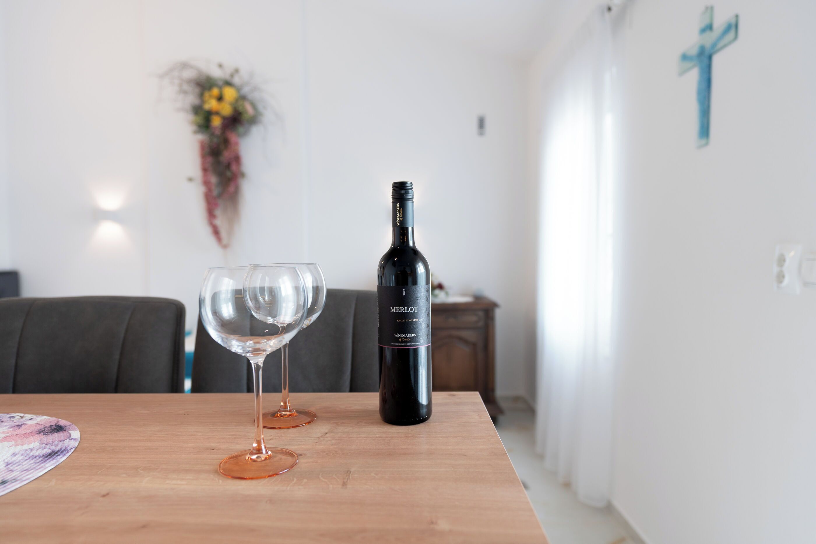 A dining table with two wine glasses and a bottle of Merlot wine.