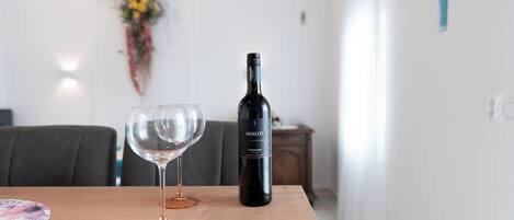 A dining table with two wine glasses and a bottle of Merlot wine.