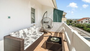 Ein Balkon mit einer Rattan-Couch, einem Hängesessel und einem kleinen Tisch.