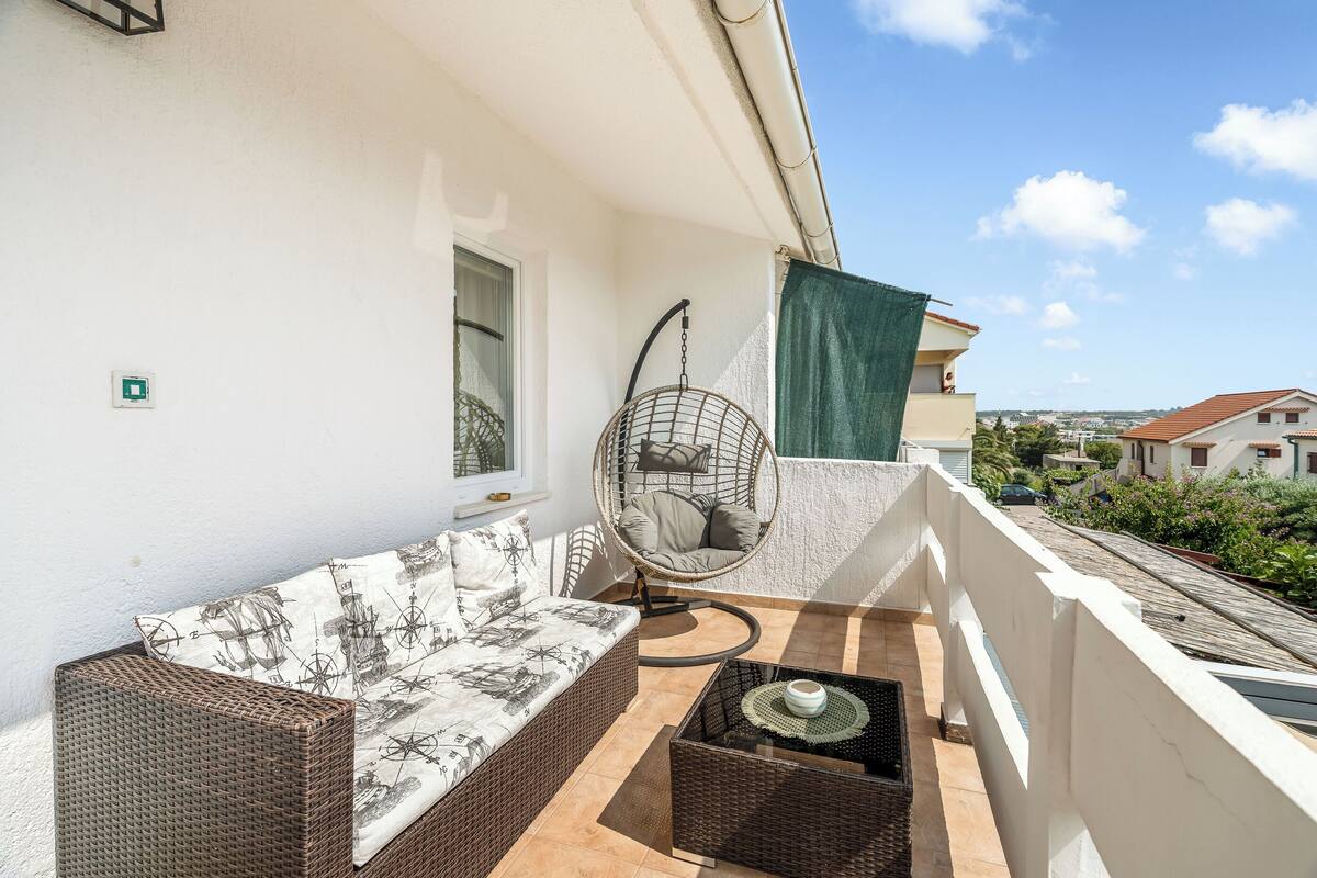 A balcony with a wicker sofa, a hanging chair, and a small table.