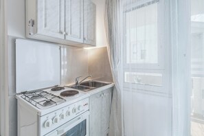 A kitchen with white cabinets, a stove, and a sink. - Apartments Jozefina (Novalja)