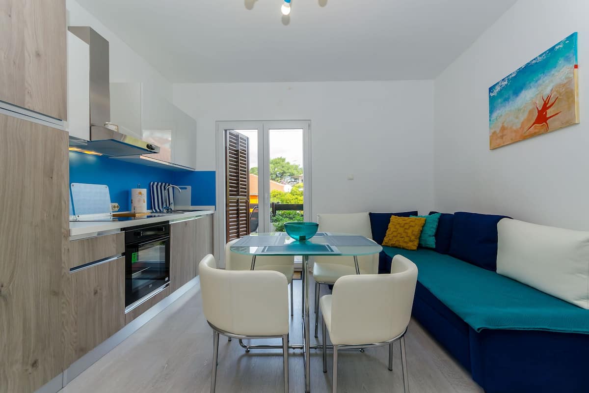 A modern kitchen with a glass dining table, white chairs, and a teal sofa.
