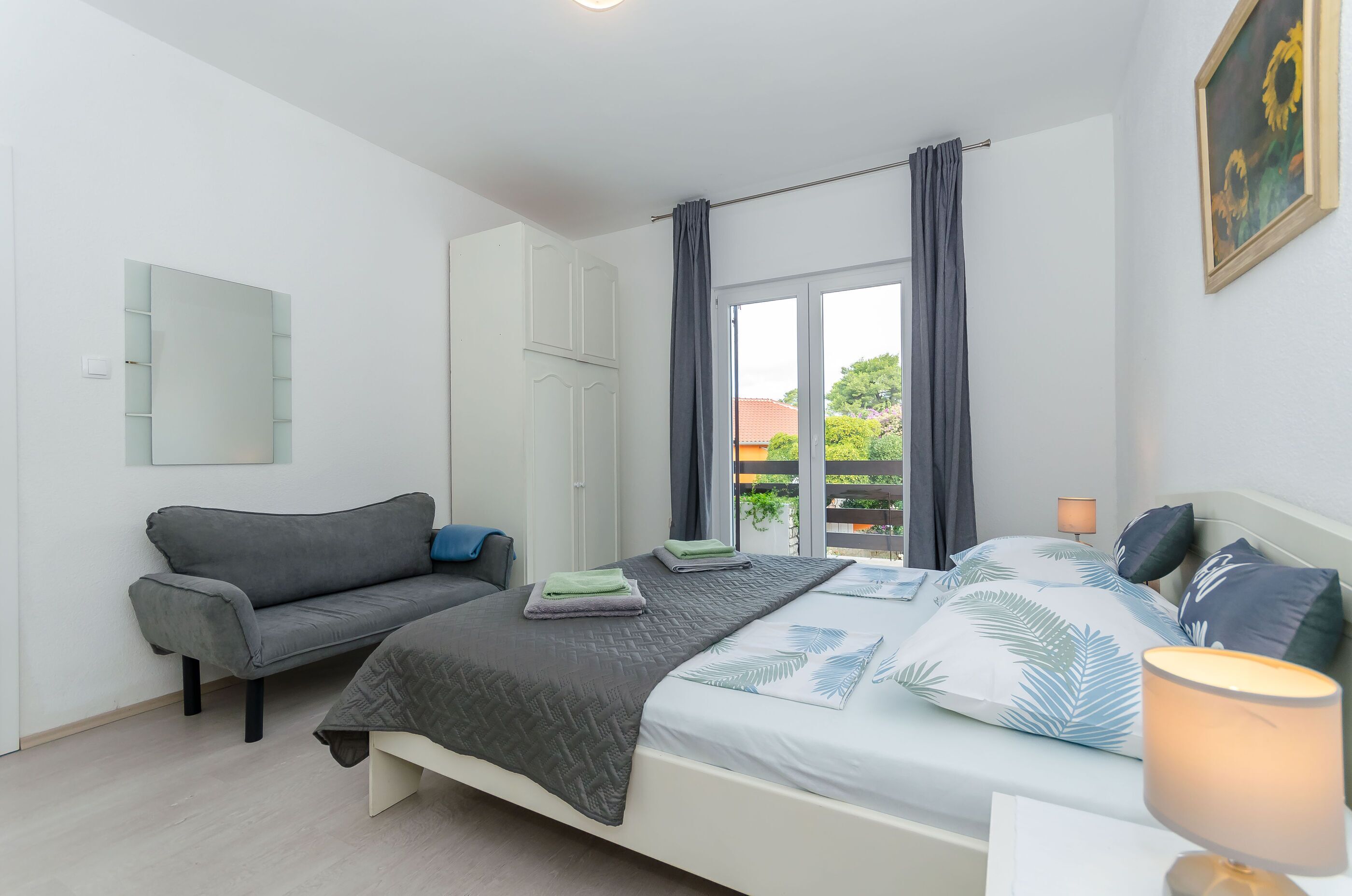 Un dormitorio con cama, sofá, espejo y ventana con cortinas.