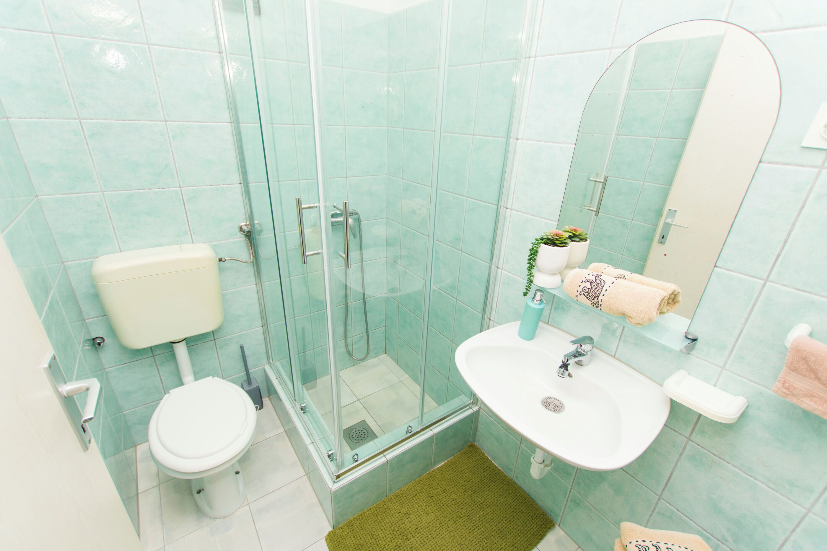 Un baño con cabina de ducha de vidrio, inodoro, lavamanos y espejo.