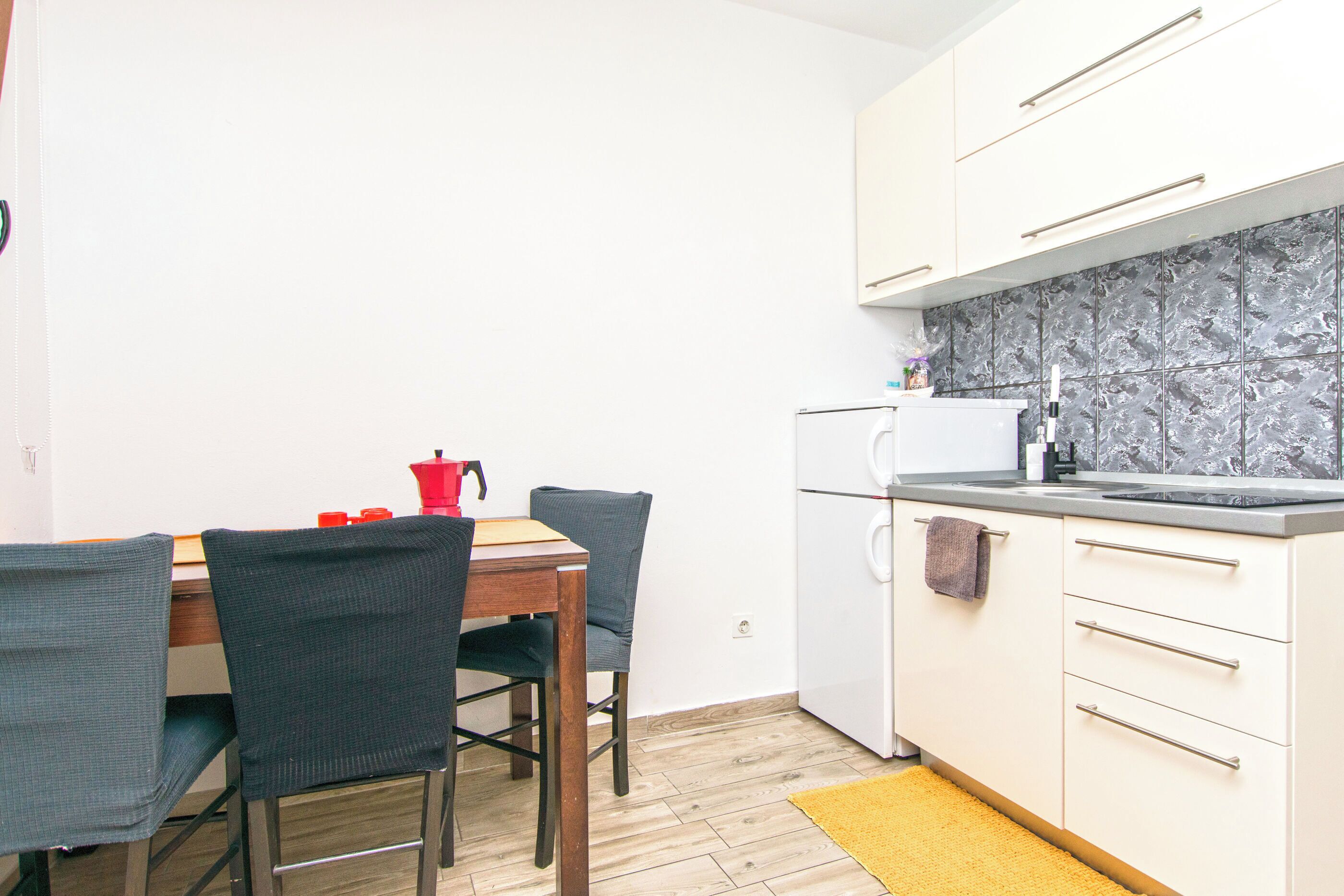 Cozinha compacta com mesa, cadeiras, geladeira e micro-ondas.