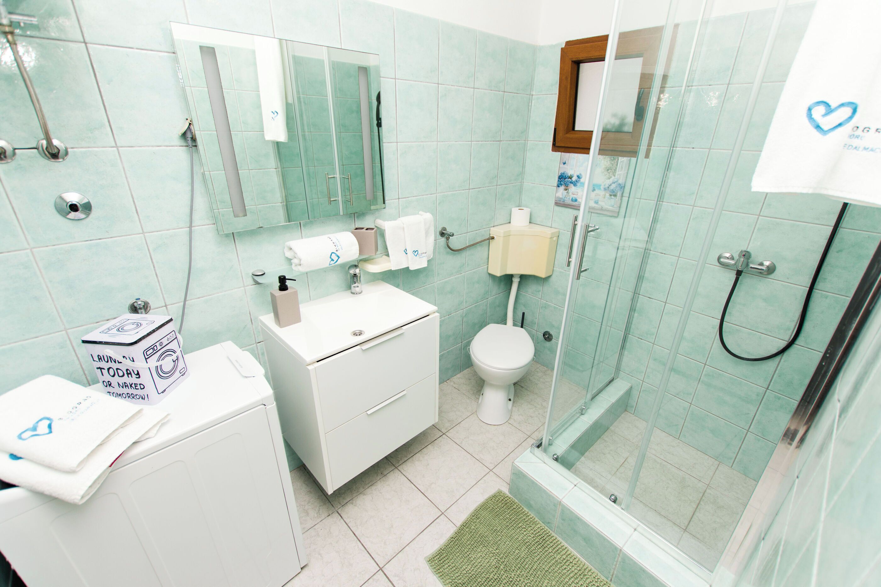 A bathroom with a glass shower enclosure, a toilet, a sink with a mirror, and a small cabinet.
