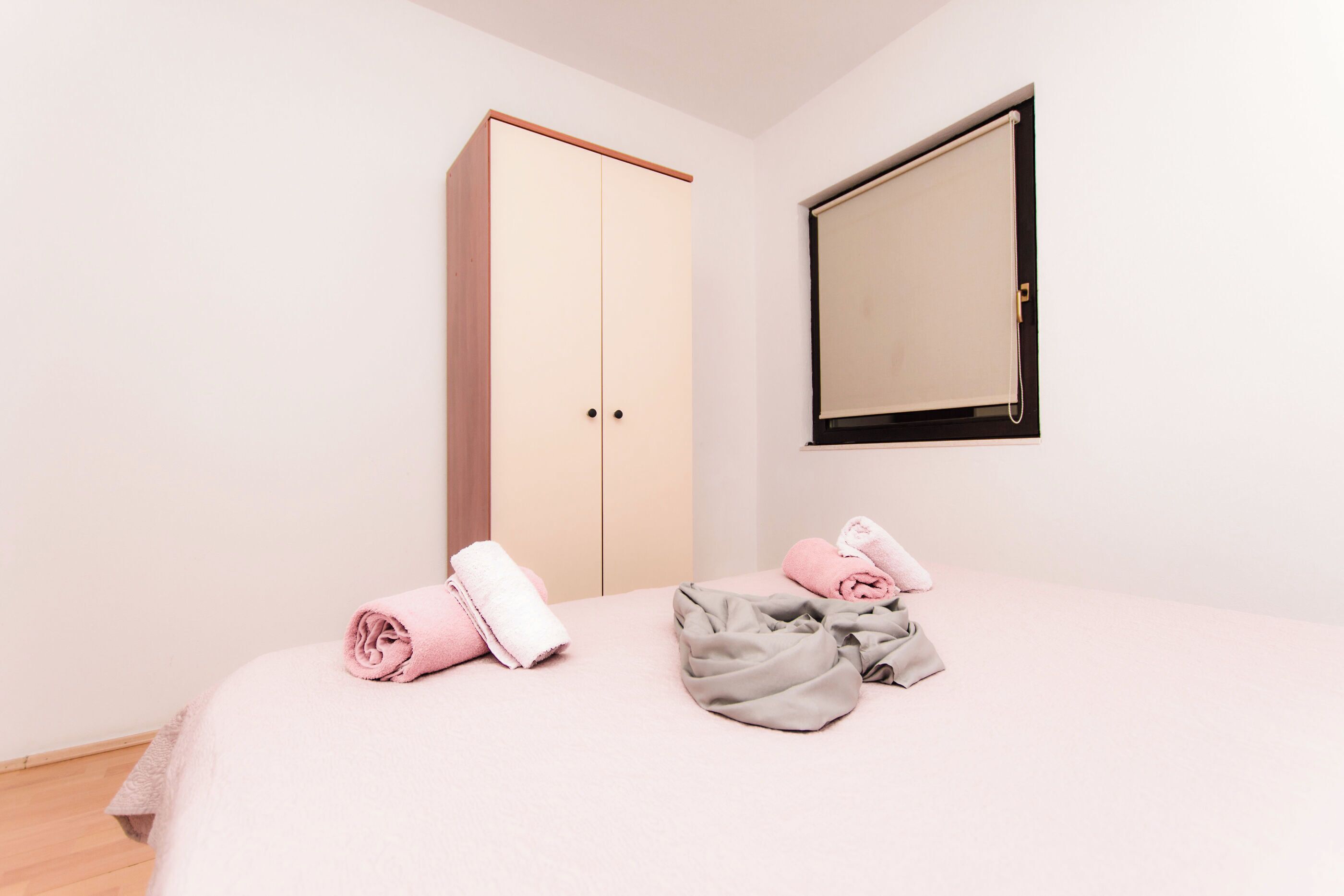 A bedroom with a bed, two rolled towels, a wardrobe, and a mirror.