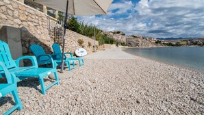 A pebble beach with turquoise chairs and a beach umbrella. - Apartments Sol Desire (Novalja)