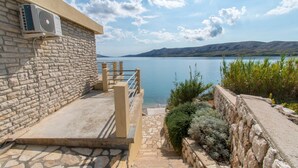 A stone building with a stone staircase leading to a balcony overlooking a lake. - Apartments Sol Desire (Novalja)