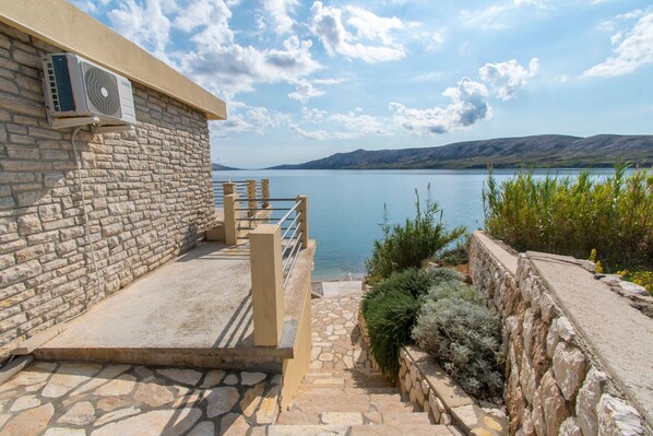 A stone building with a stone staircase leading to a balcony overlooking a lake. - Apartments Sol Desire (Novalja)