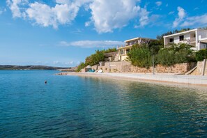 A coastal property with a stone retaining wall, a clear blue sea, and a white building with balconies. - Apartments Sol Desire (Novalja)