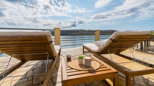 A wooden deck with two lounge chairs and a table, overlooking a body of water and distant hills. - Apartments Sol Desire (Novalja)
