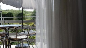 Eine Terrasse im Freien mit Tisch und Stühlen, einem großen Sonnenschirm und Blick auf Grünflächen.