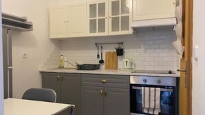 A compact kitchen with white upper cabinets, a grey countertop, a built-in oven, and a dining table with chairs. - Apartments Lion (Umag)