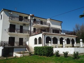 A two-story building with a balcony on the upper floor, a small garden area in front, and a sign indicating the name 'MAY'. - Apartments Lion (Umag)