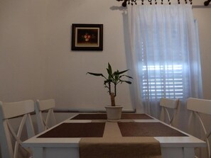 Un coin repas comprenant une table, des chaises, une plante en pot et un tableau encadré accroché au mur.