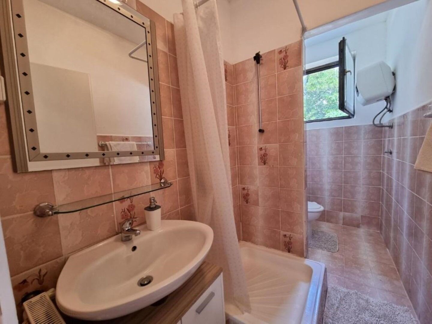 A bathroom with a sink, mirror, shower, and toilet.