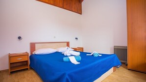 A bedroom with a wooden headboard, a blue bedspread, two bedside tables, a radiator, and a wooden wardrobe. - House Country (Omis)