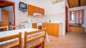 A compact kitchen with wooden cabinets, a tiled backsplash, a stove, and a small television. - House Country (Omis)