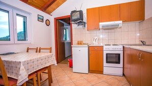A compact kitchen with wooden cabinets, a white refrigerator, a stove, and a television on a wooden beam. - House Country (Omis)