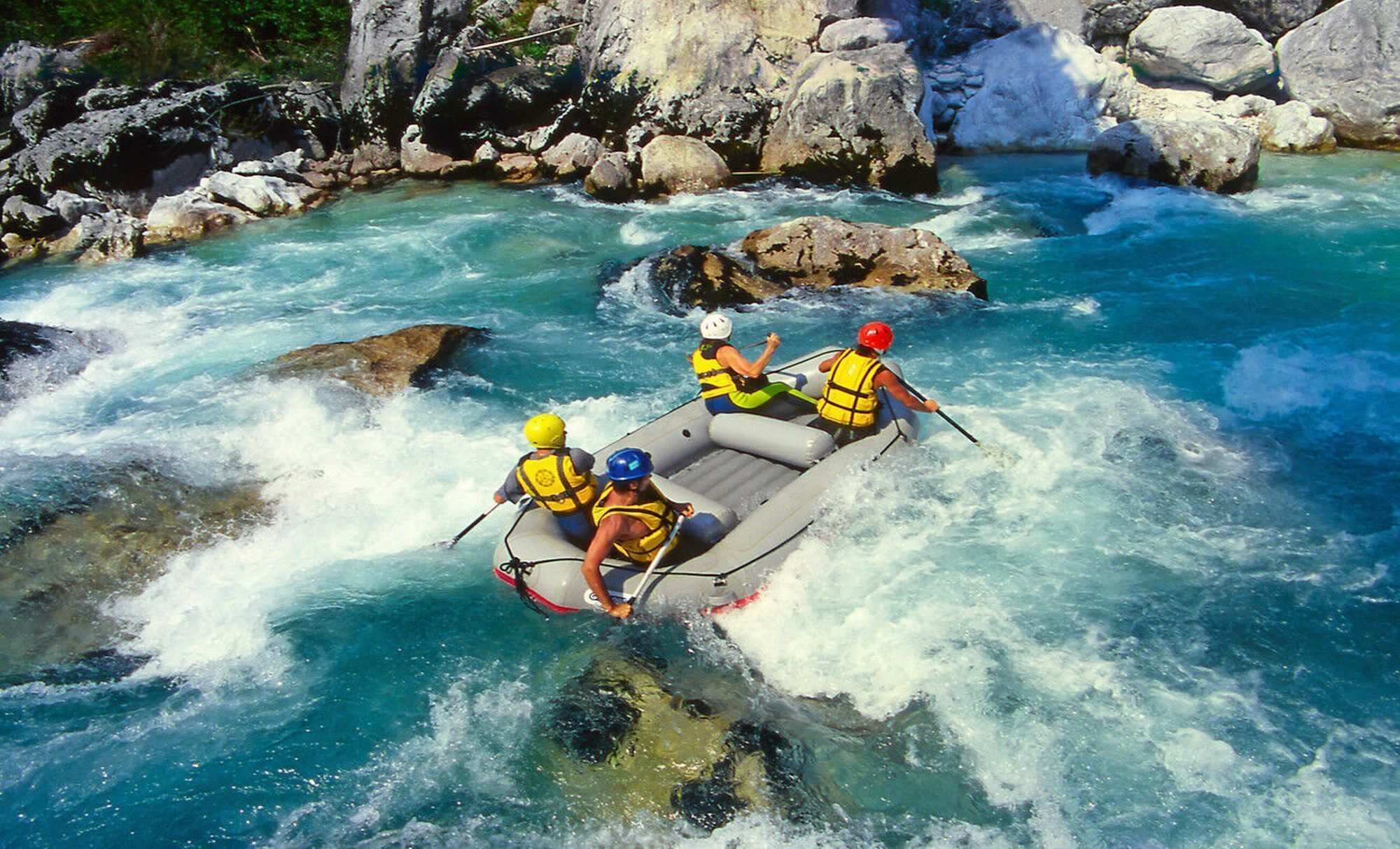 A group of people in a raft navigating a river with clear water and rocky surroundings.