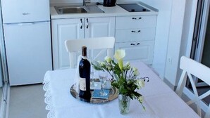 Una cocina pequeña y blanca con una mesa de comedor para dos personas, un refrigerador y una ventana.