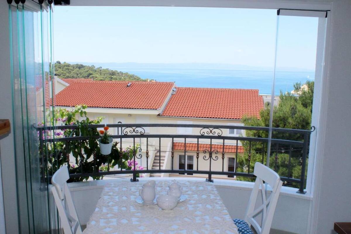 Un balcon avec une table et des chaises, offrant une vue sur la côte, avec des bâtiments et un ciel dégagé.