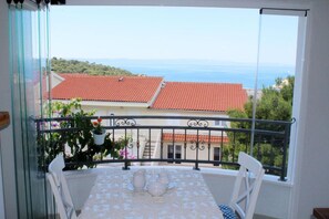 A balcony with a table and chairs, overlooking a coastal view with buildings and a clear sky. - Apartments Adriona (Makarska)