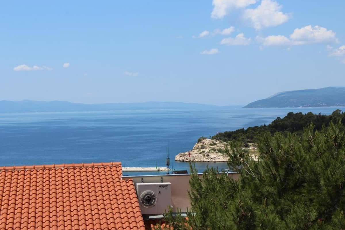 Une vue sur la côte, avec un toit recouvert de tuiles, un bâtiment doté d’un appareil de climatisation et une ligne de rivage lointaine.