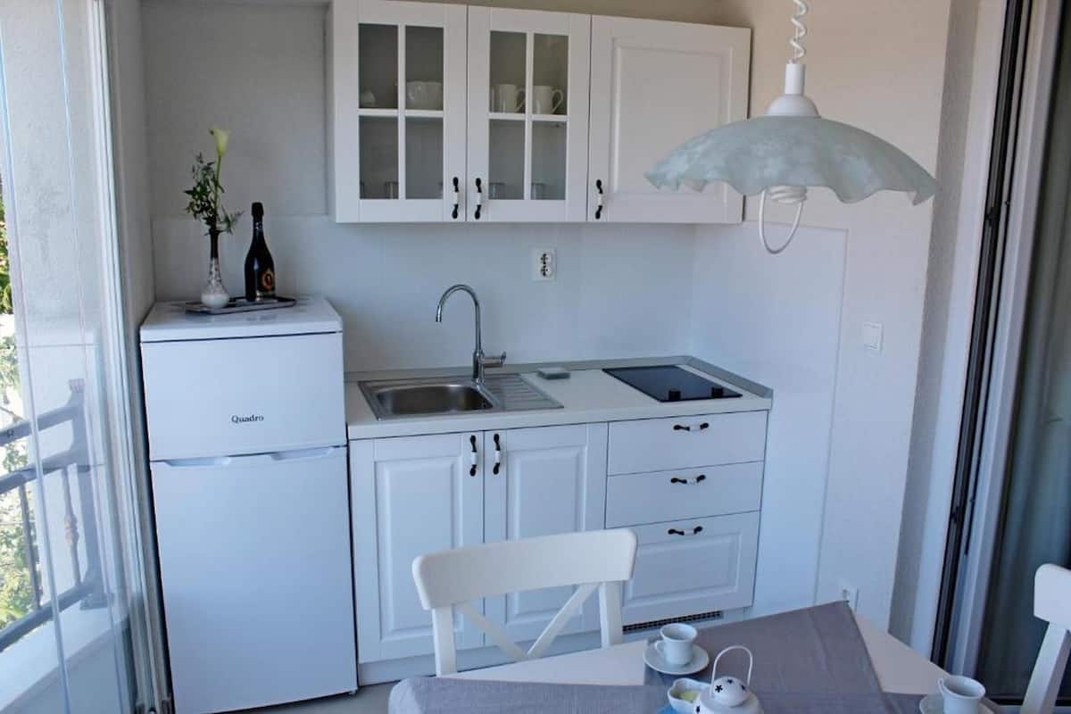 Une cuisine compacte avec des meubles blancs, un évier, un réfrigérateur et un coin repas comprenant une table et une chaise.