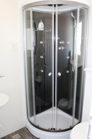A corner shower enclosure with a glass door, a handheld showerhead, and a bottle of shampoo. - Apartments Adriona (Makarska)