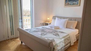Een slaapkamer met een bed, nachtkastje, lamp en raam met zonwering.