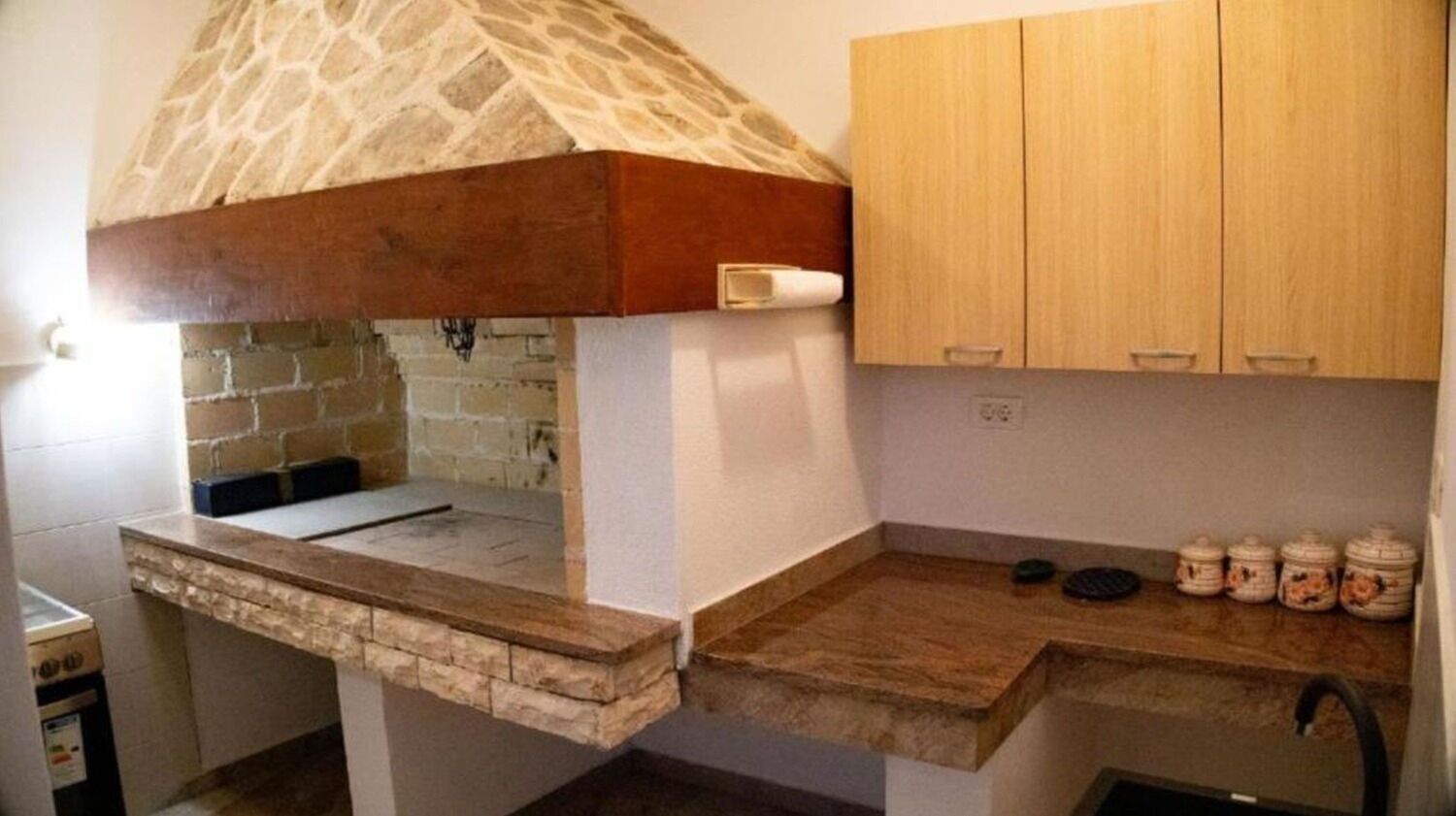 A kitchen with a stone oven, wooden cabinets, and a countertop with jars.