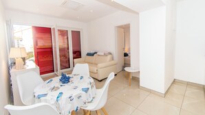 A bright living room with a white table set for dining, a beige sofa, and a red-framed sliding door. - Apartment Dora Pag (Pag)